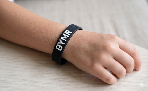 Black wristband with 'GYMR' on a person's wrist against a neutral background