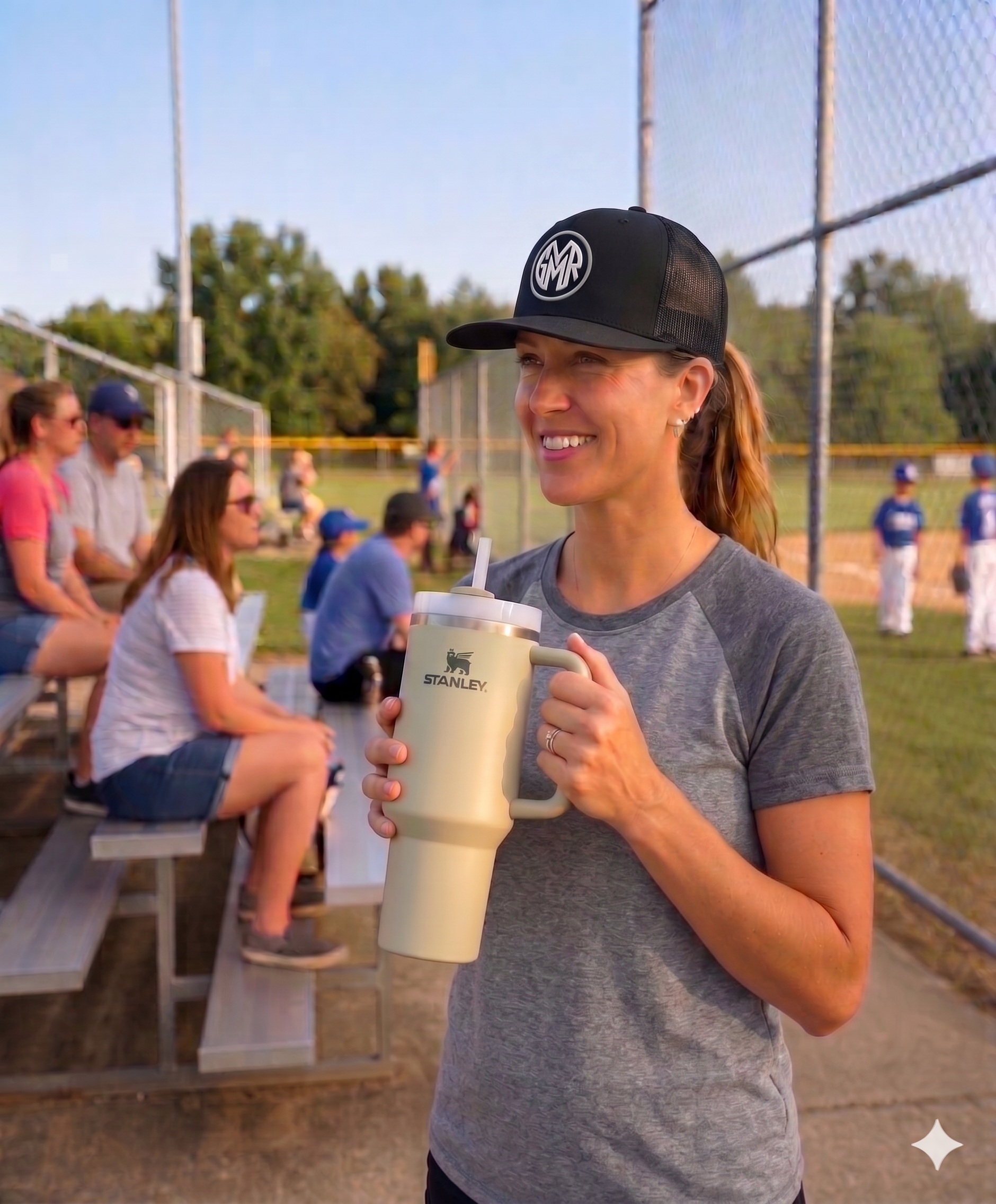 Woman wearing a GYMR black hat at a baseball game with people in the background
