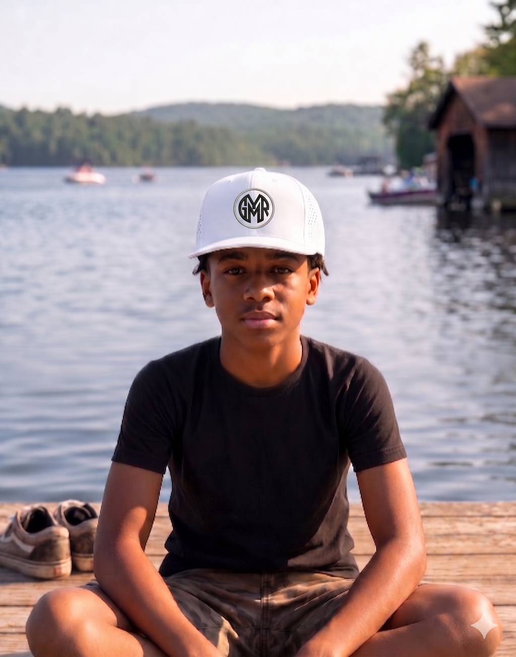 Person sitting on a dock by a lake wearing a white cap GYMR hat